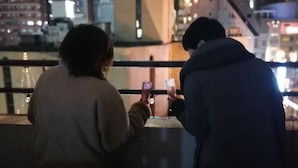 Deux personnes sont assises sur un balcon, d’où elles contemplent une vue nocturne sur la ville.