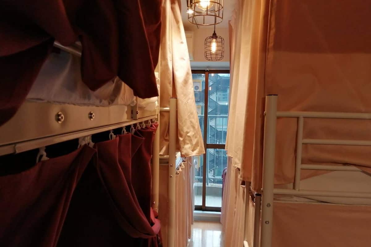 Un couloir étroit, avec des lits superposés d’un côté et une fenêtre au fond.