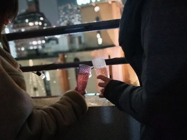 A person holding a glass with a textured pattern, standing near a railing with a cityscape in the background.