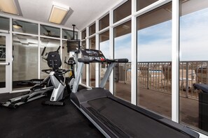 A gym with a treadmill, elliptical, and stationary bike, large windows with a view of a pool and outdoor area.