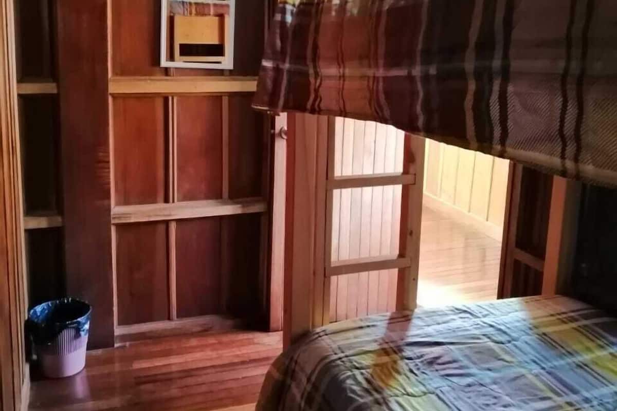 A bunk bed with a plaid blanket, wooden walls, and a small shelf unit.