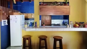 A kitchen with a white refrigerator, wooden cabinets, a yellow wall, and three stools. - Sofi's Hostel Monteverde (Sierra)
