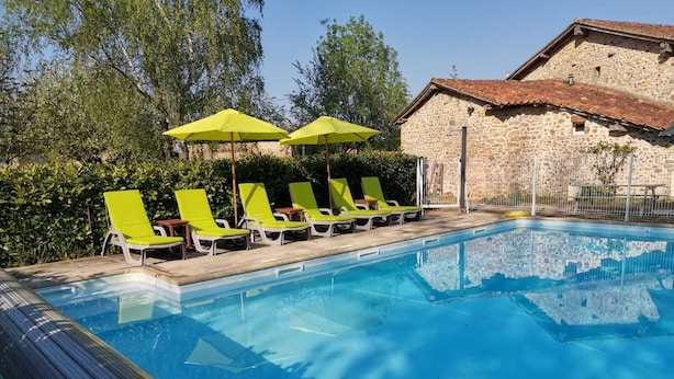 A swimming pool with green lounge chairs and umbrellas, surrounded by greenery and a stone building. - 3 Bedroom  character property (L'Âge)