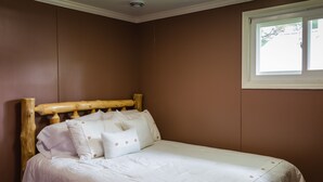 Un lit bien fait, avec une tête de lit en bois et une literie blanche, dans une pièce aux murs marron et dotée d’une fenêtre.