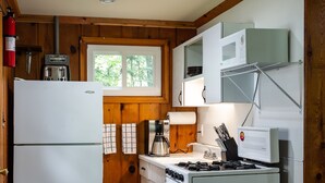 Une cuisine compacte équipée d’un réfrigérateur, d’une cuisinière, d’un four à micro-ondes et de meubles de rangement en bois.