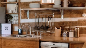 A kitchen with wooden cabinets, a stainless steel dishwasher, and hanging utensils. - Beautiful and Historic Log Cabin: cozy, quiet, huge hot tub! Quiet getaway! (Goshen)