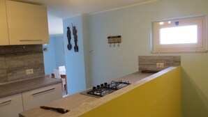 A kitchen with light blue walls, a yellow accent wall, wooden cabinets, a gas stove, and a window with natural light. - Casa Martina Appartamento Panoramico (Terracina)