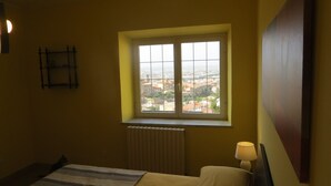A bedroom with a window overlooking a cityscape, a bed, a bedside table with a lamp, and a radiator. - Casa Martina Appartamento Panoramico (Terracina)