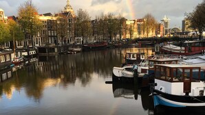 Un canal où sont amarrés des bateaux, un arc-en-ciel dans le ciel et des bâtiments en arrière-plan.