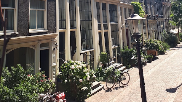 Une rangée de bâtiments de style européen traditionnel, caractérisés par des façades uniformes, de grandes fenêtres et une rue pavée de briques.