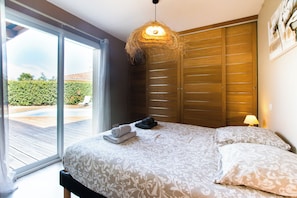 Een slaapkamer met een bed, een hanglamp, een schuifdeur en uitzicht op het groen.