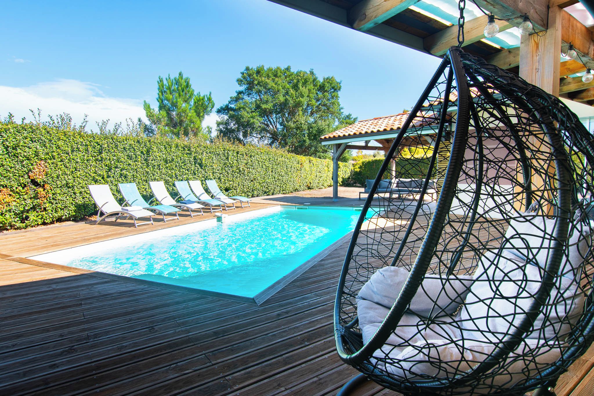 Una piscina con sillones de descanso y una hamaca colgante.