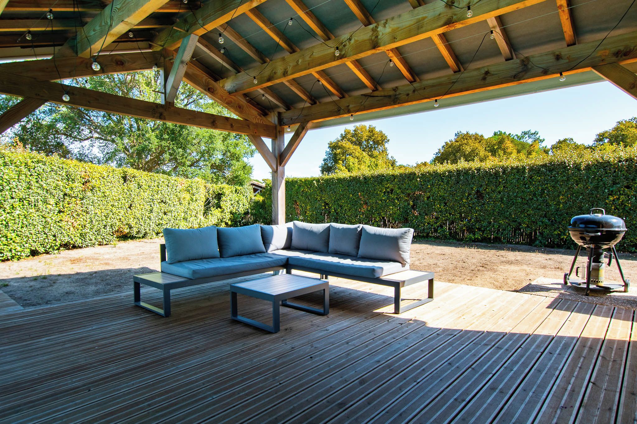 Un espacio de estar techado al aire libre con terraza de madera, sofá modular y una parrilla.