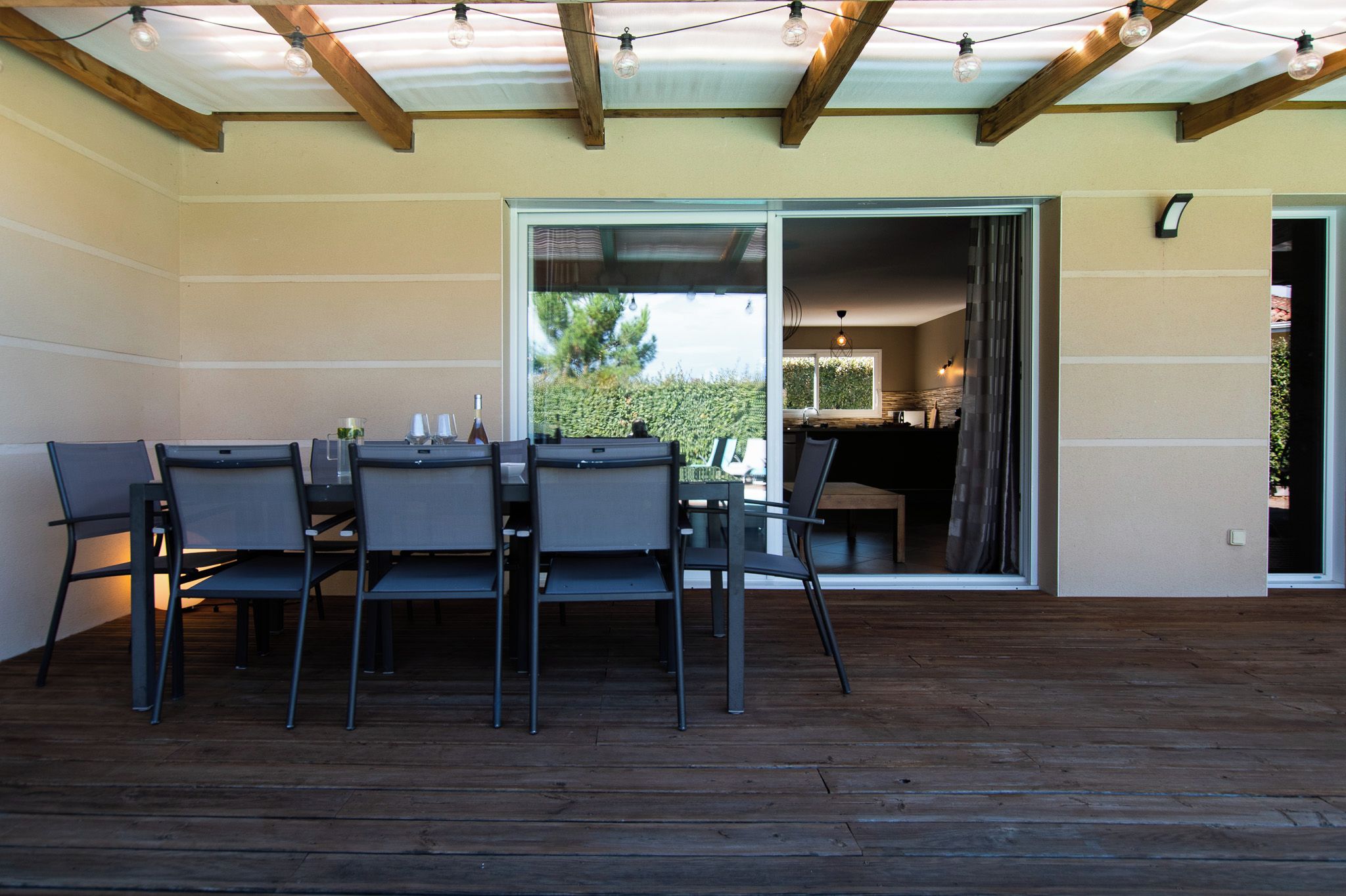 Un patio exterior con terraza de madera, una mesa con sillas y un ventanal corredero que da a un espacio interior.