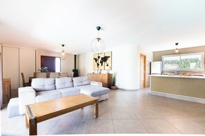 Een moderne woonkamer met een hoekbank, een houten salontafel, een wereldkaart kunstwerk en een keukenhoek met een spoelbak en aanrecht.