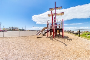 Children can play safely on the playground's soft surface, surrounded by a fence and a nearby residential building.