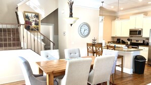 A spacious kitchen with modern appliances, a dining area with a wooden table and upholstered chairs, and a staircase leading to another level.