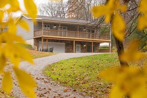 A two-story house with a stone foundation, a wooden deck, and a covered front porch.