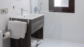 A modern bathroom with a white sink, mirror, and shower. There is a window above the shower and a towel rack with towels.