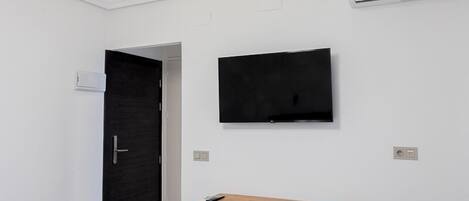 Une chambre moderne dotée d’un téléviseur à écran plat fixé au mur, d’un bureau en bois avec une chaise et d’une porte sombre.
