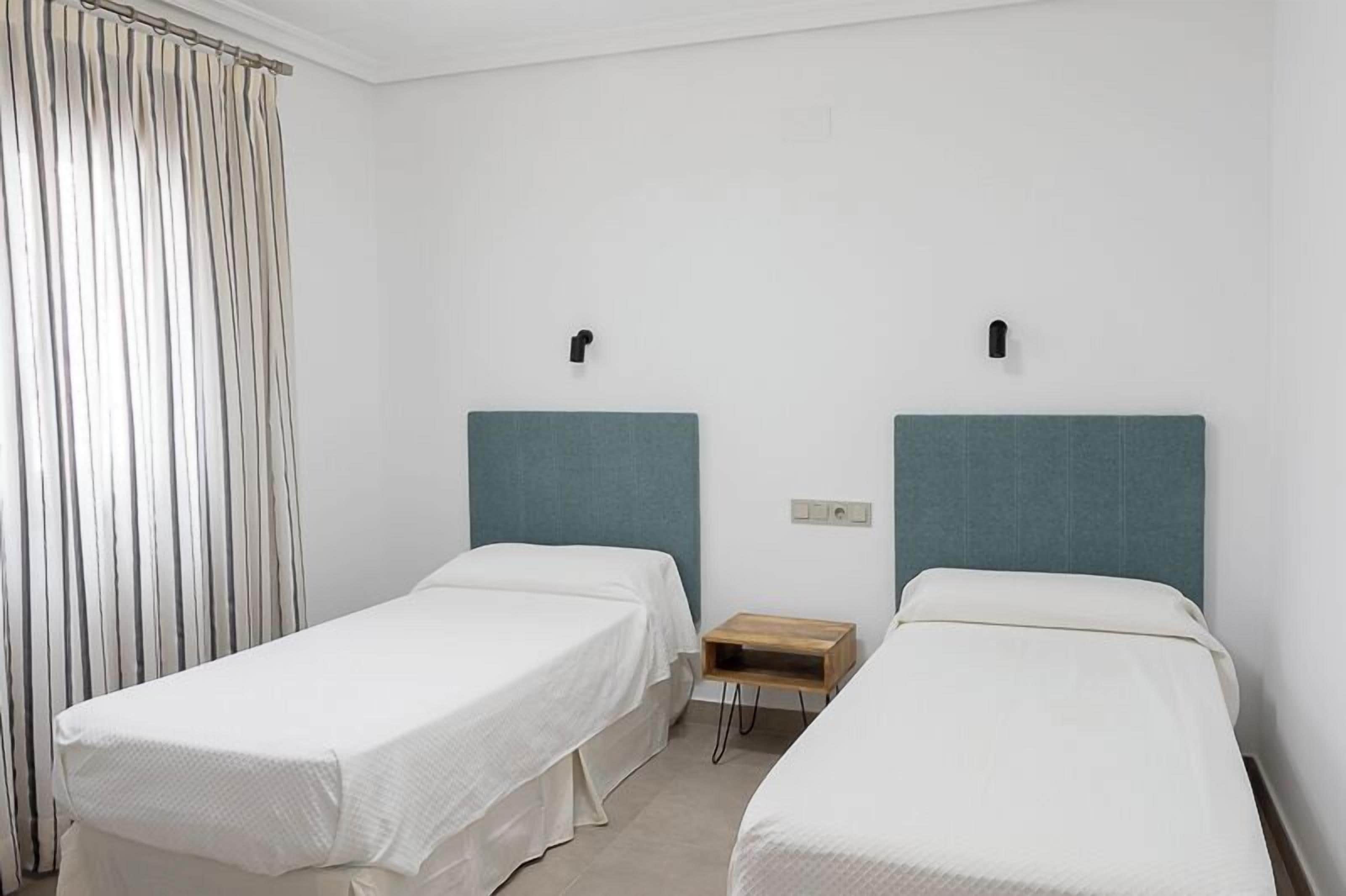 A hotel room with two single beds, a wooden nightstand, and a window with curtains.