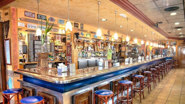 Un bar con una barra alargada, varios taburetes y diferentes letreros y adornos.