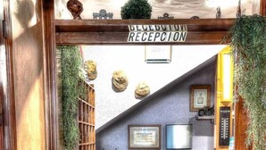 Un área de recepción con un mostrador de madera, un letrero encima y un mostrador con una computadora y una caja registradora.