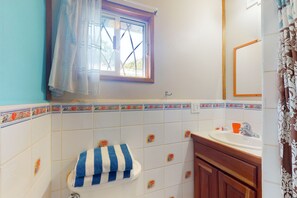 Bathroom features a window above the toilet, a decorative tile border, a sink area with a cabinet and mirror.