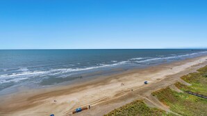A wide beach with a clear sky, a few people, and a distant pier.