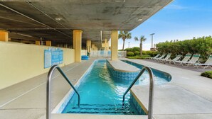 A swimming pool with a lifeguard station, lounge chairs, and a pool rules sign.