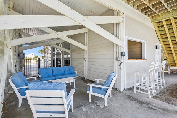A covered outdoor seating area with white furniture, a blue sofa, and a small table.