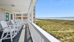 A balcony with white chairs and a view of the beach.