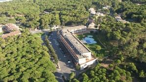 Vista aérea de un hotel con estacionamiento, piscina y zona boscosa circundante.