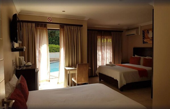 A hotel room with a bed, a desk, and a chair. There is a window with curtains, and a view of a pool outside.