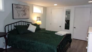 A neatly arranged bedroom with a bed, a bedside table with a lamp, a framed motivational quote on the wall, and a door with a mirror.