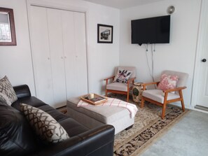 Un salon comprenant un canapé, deux fauteuils, une table basse, un téléviseur et un tapis à motifs.