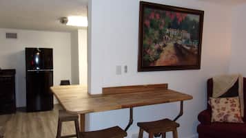 Ein Essbereich mit einem Holztisch, zwei Hocker, einem schwarzen Kühlschrank und einem Gemälde an der Wand.