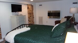 A bedroom with a green bed, a TV mounted on the wall, a lamp, and a chair. - The Commuter's Dream. This location is close to you destination. (Chattanooga)