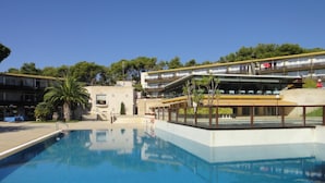 Ein Swimmingpool mit glatter, blauer Wasseroberfläche, umgeben von einem Gebäude mit mehreren Balkonen und einem überdachten Bereich mit Sitzgelegenheiten.