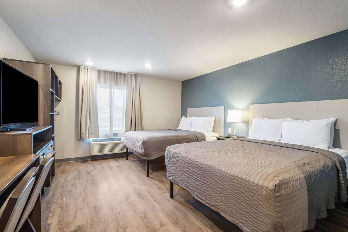 Habitación de hotel con dos camas, televisor, escritorio y ventana con cortinas.