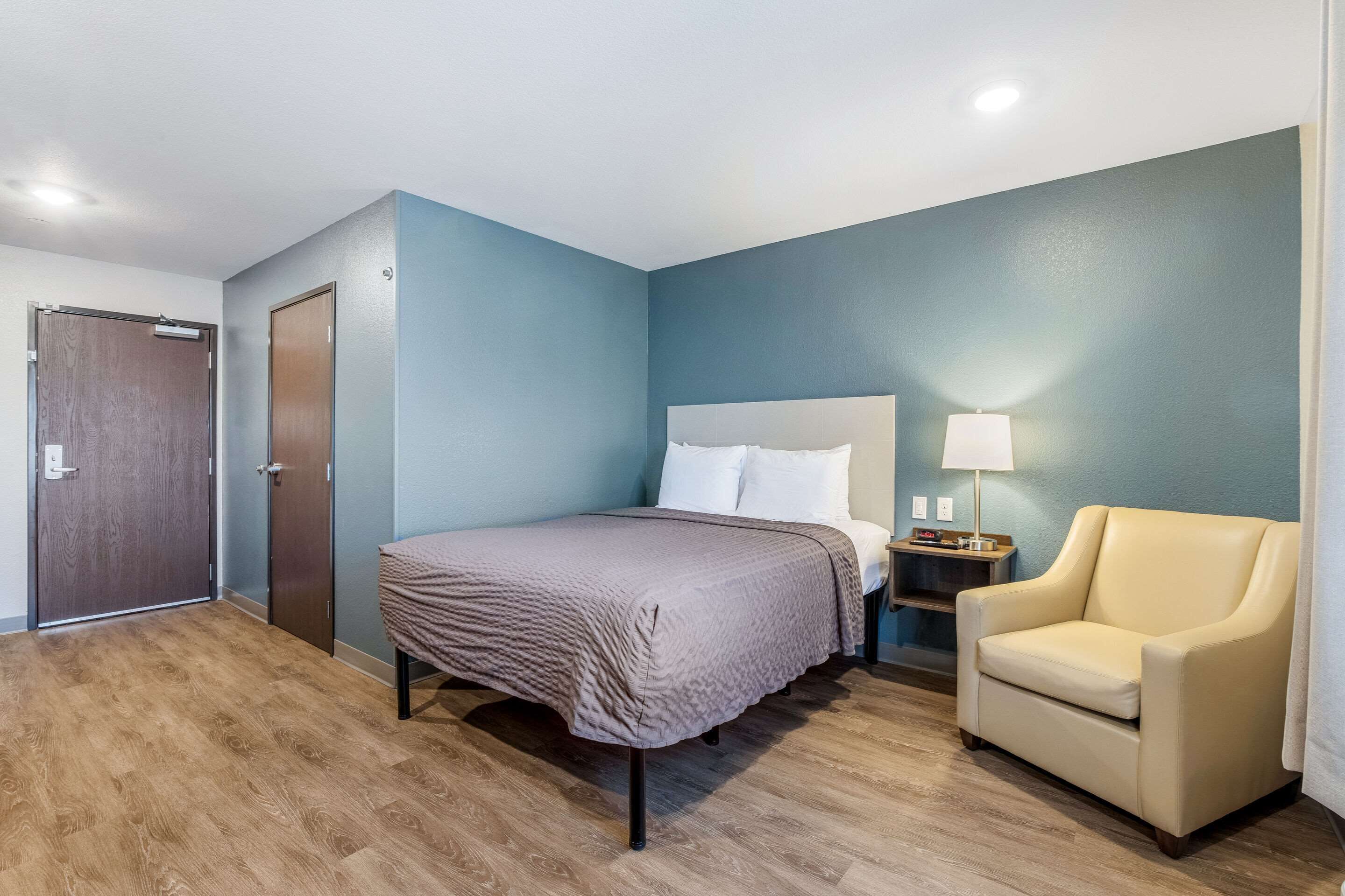 Una habitación de hotel con cama, silla, mesita de noche y puerta.