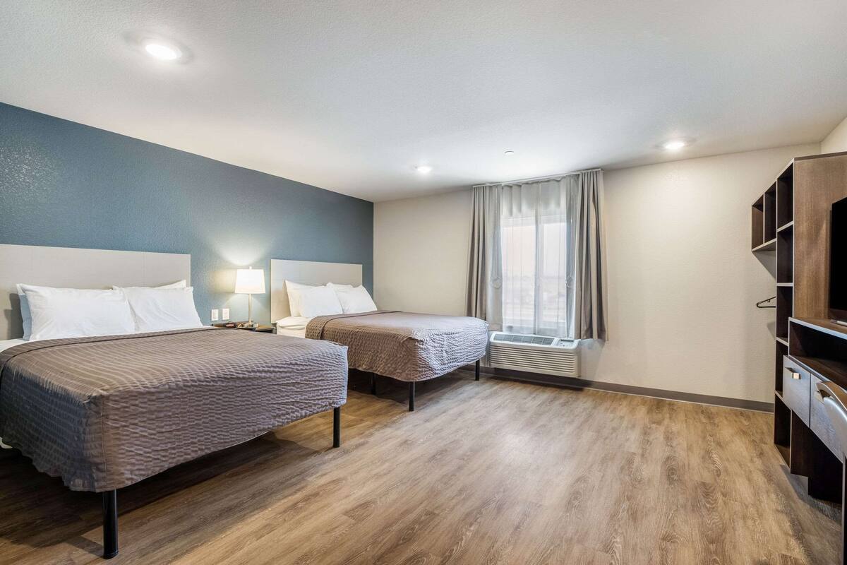 Habitación de hotel con dos camas, un escritorio, una silla y un televisor.