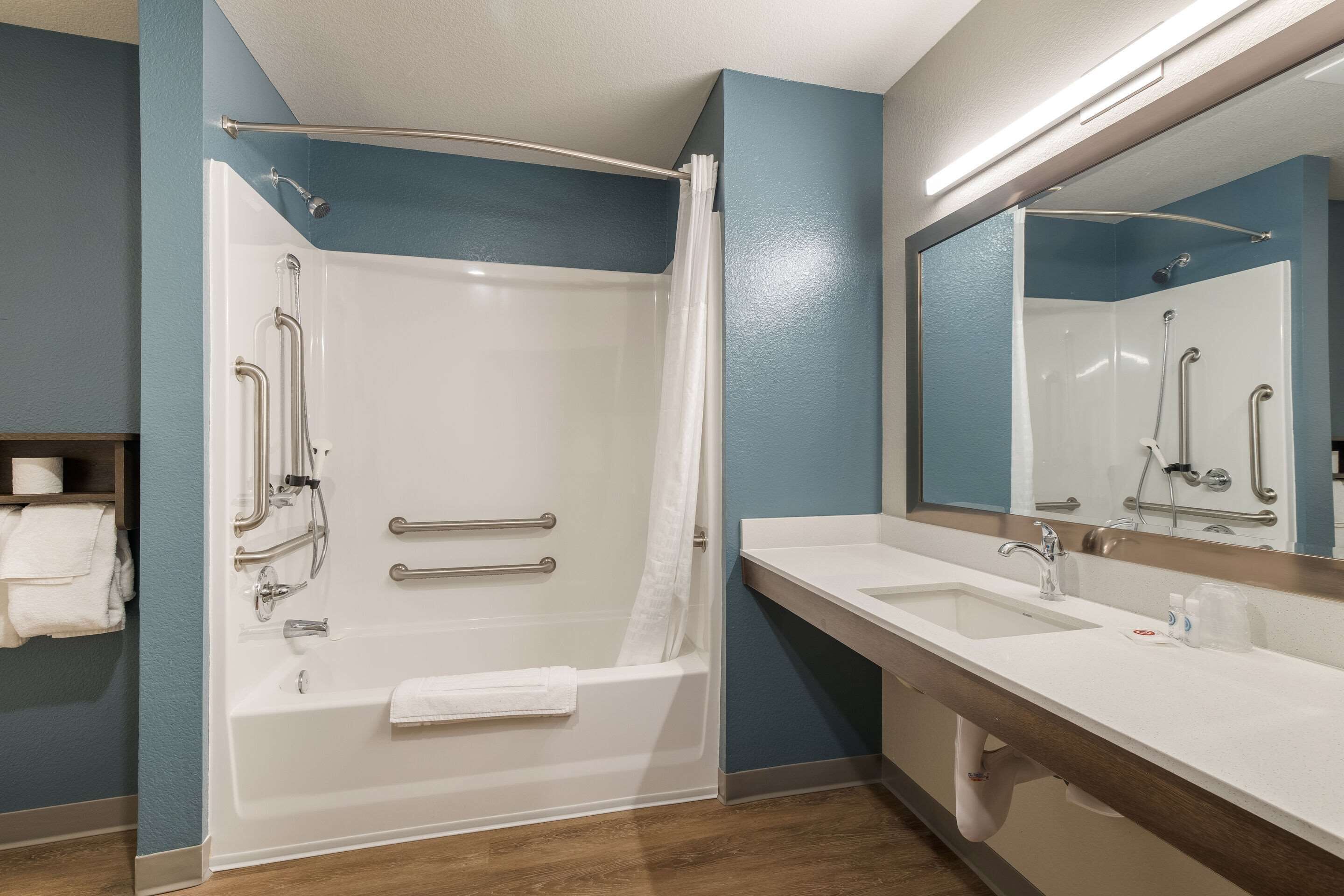 A modern bathroom with a walk-in shower, grab bars, a sink, and a mirror.