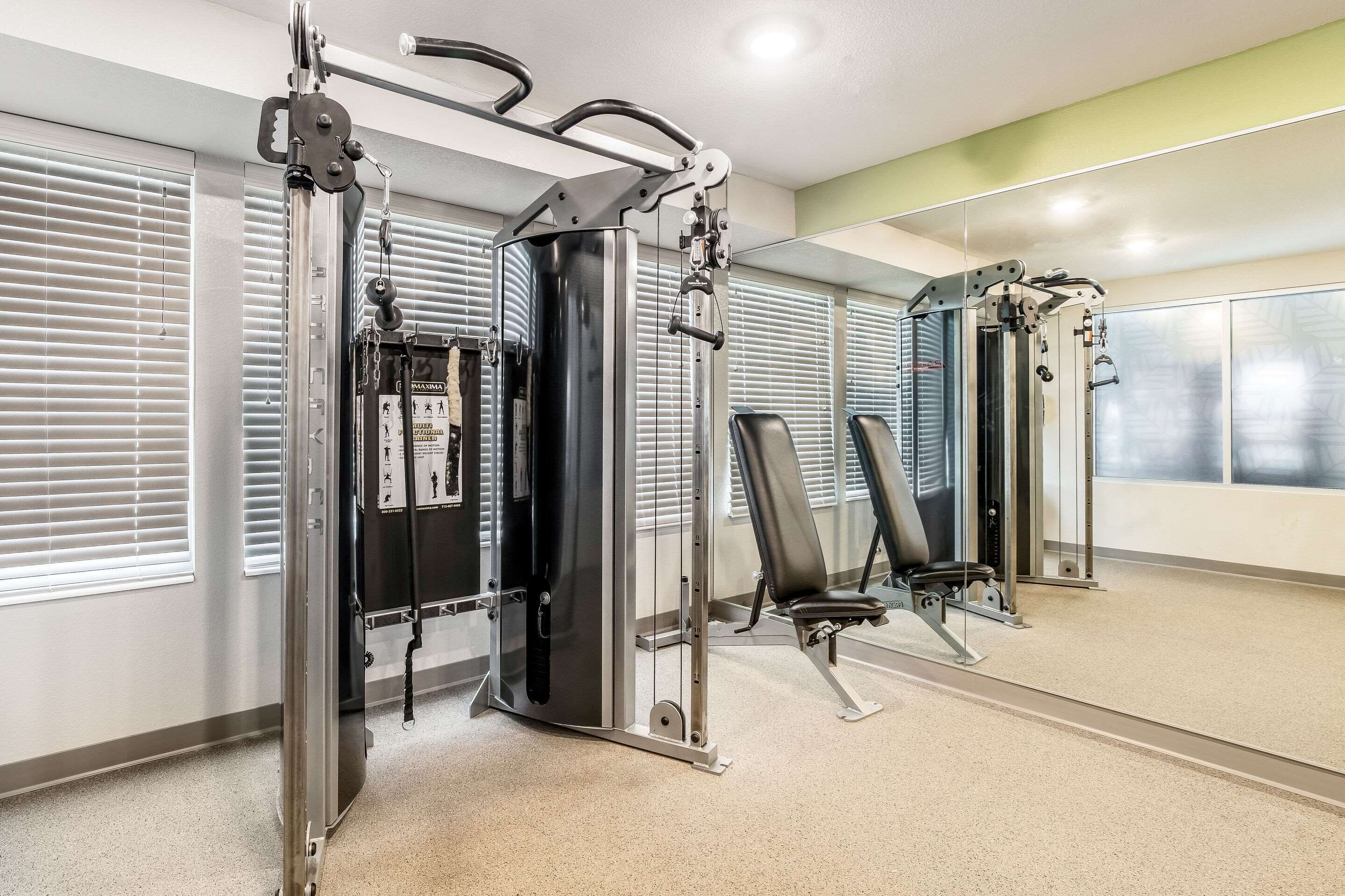 A gym with exercise machines, a mirror, and a window with blinds.
