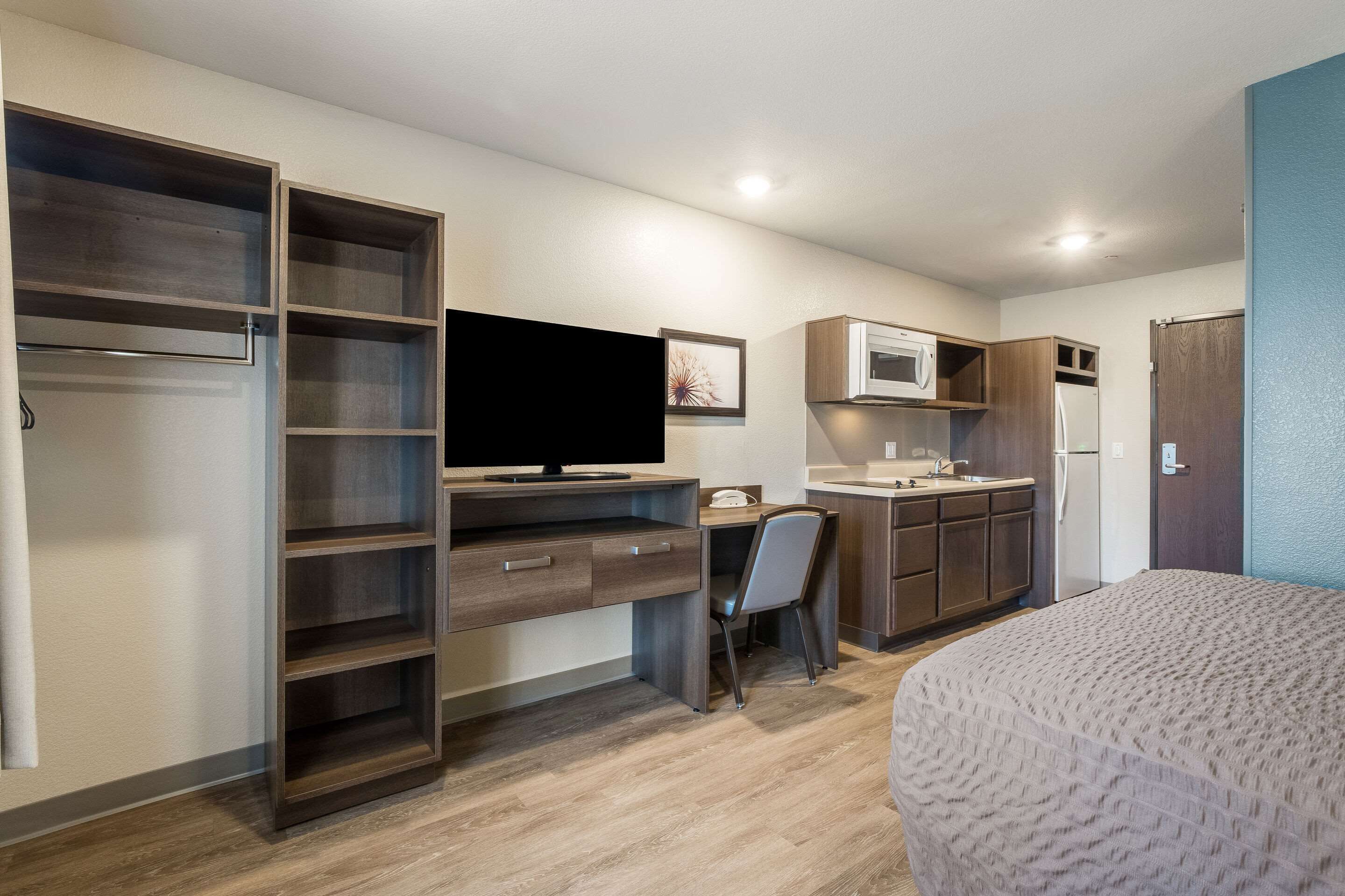 Ein gemütliches Zimmer mit Bett, Schreibtisch, Stuhl, Fernseher, Mikrowelle, Kühlschrank und Kleiderschrank.