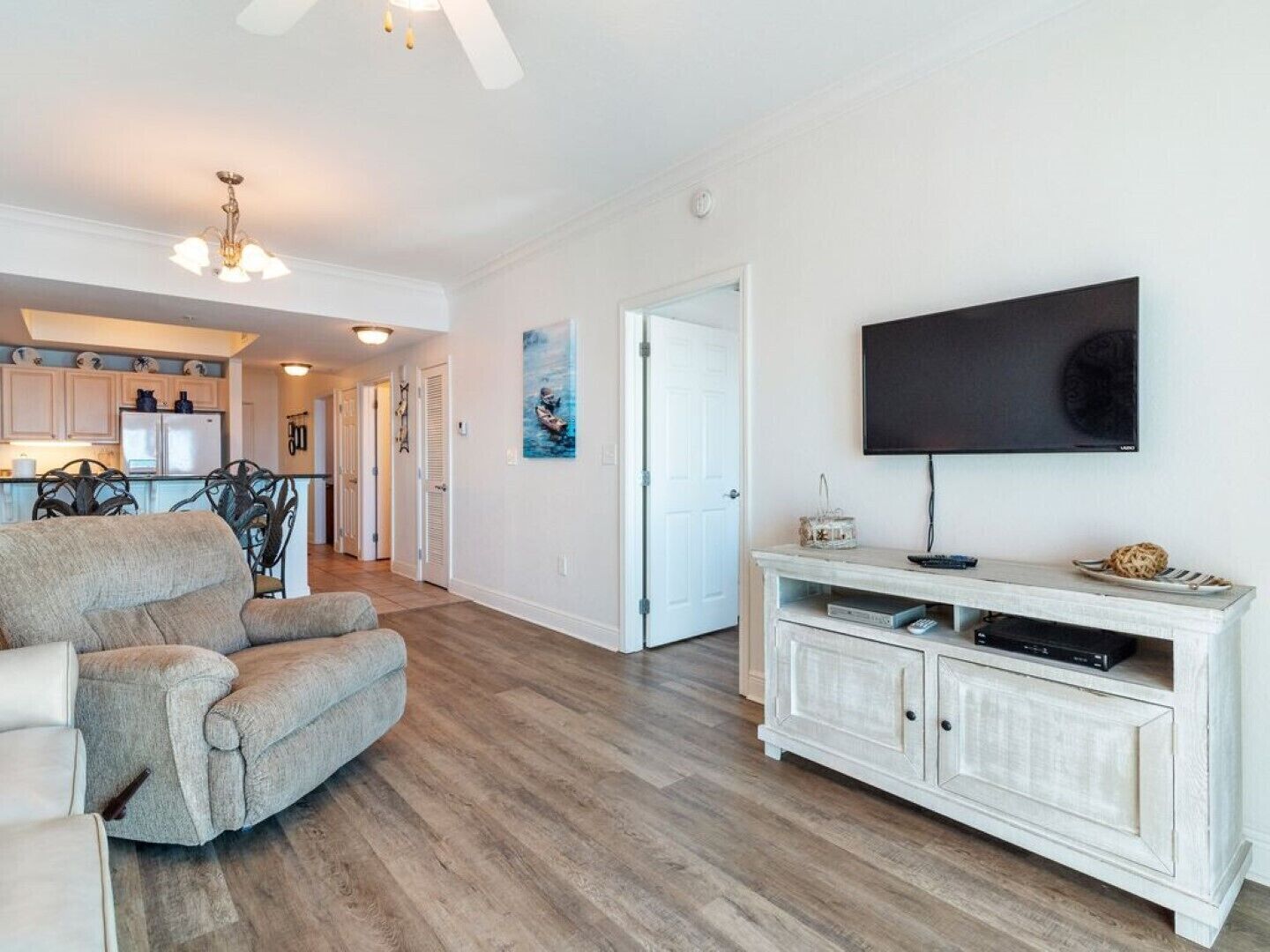 Een ruime woonkamer met een grote grijze bank, een witte tv-meubel en een houten vloer.