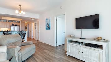 Een ruime woonkamer met een grote grijze bank, een witte tv-meubel en een houten vloer.