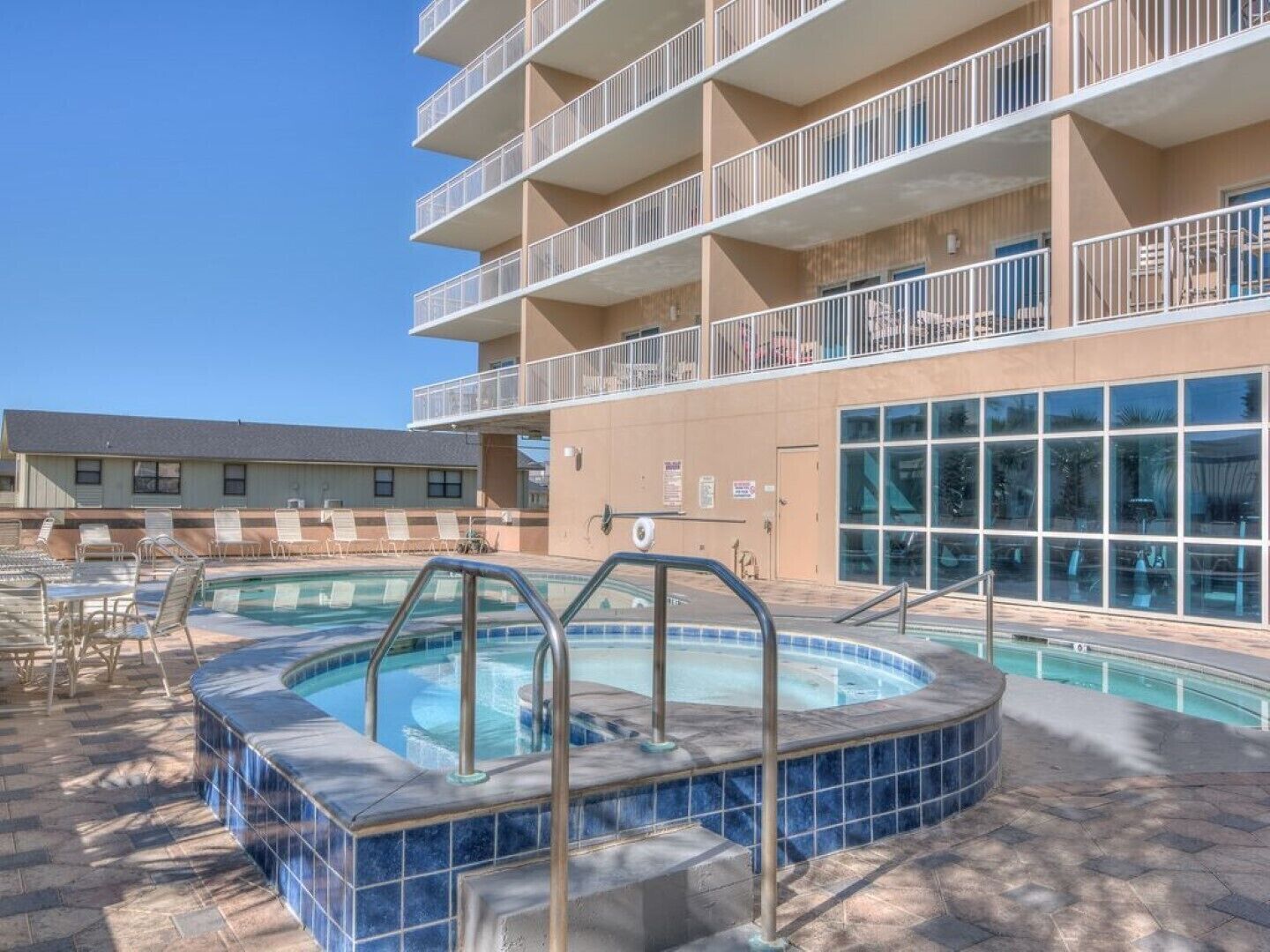 A hotel with a swimming pool, outdoor seating, and a multi-story building with balconies.