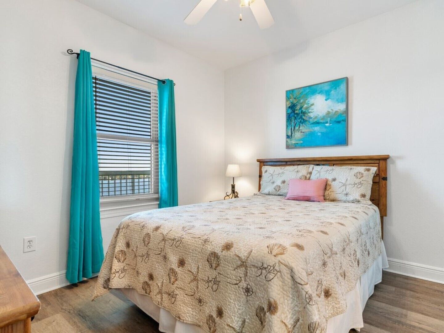 Une chambre à coucher avec un lit, une fenêtre avec des rideaux, un tableau au mur et une table de chevet avec une lampe.