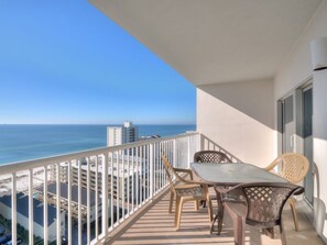 A balcony with a table and chairs, overlooking a beach and ocean.
